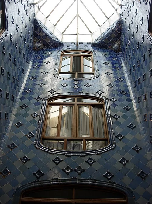 Patio di luce di Casa Batlló visto dal basso. La gradazione delle piastrelle, più intense in alto e più chiare verso il basso, compensa la diversa quantità di luce naturale e fa percepire il rivestimento come molto più uniforme di quanto sia realmente.  Foto: Mcginnly / Wikimedia Commons — CC BY-SA 3.0.